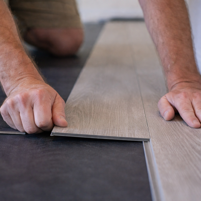 Close-up van iemand die een click-PVC plank in elkaar klikt tijdens het leggen van een vloer.