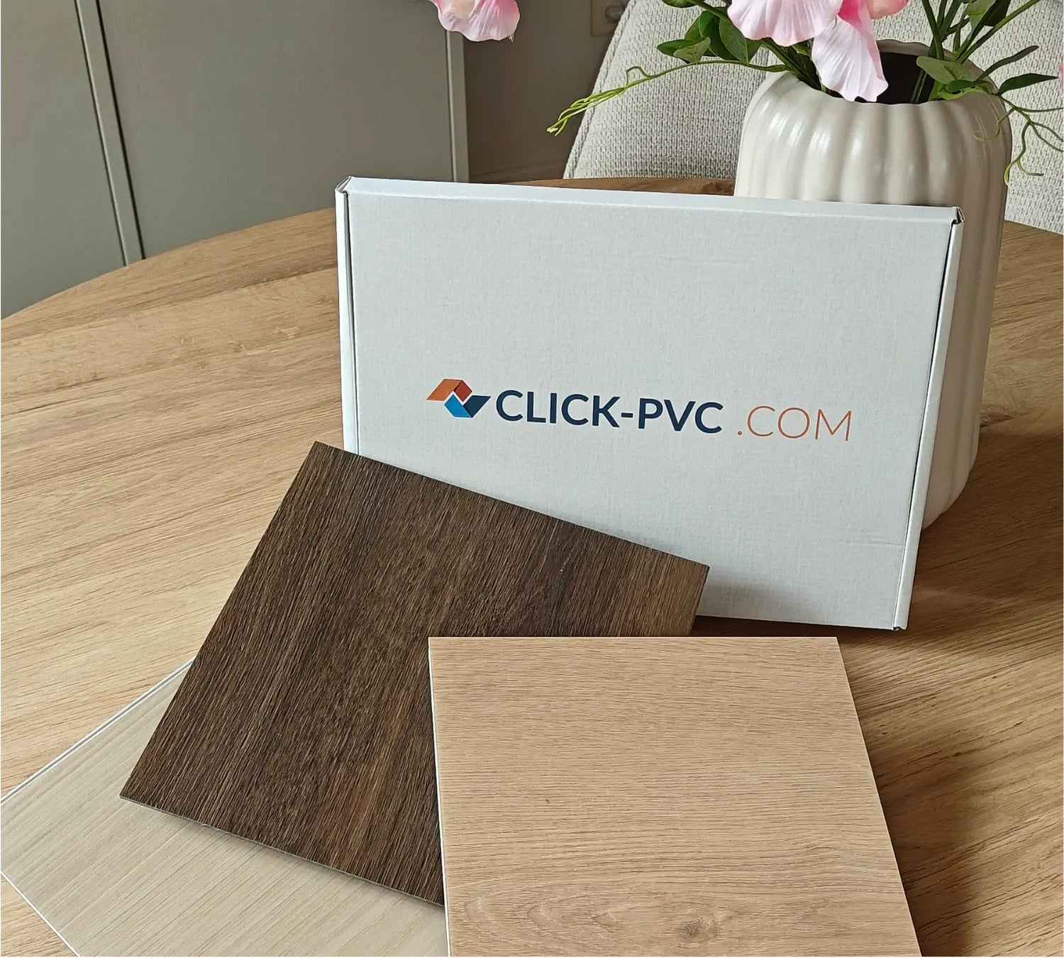 Sfeerfoto van drie gratis vloerstalen van Click-pvc.com met de bedrukte verzenddoos op een ronde houten tafel